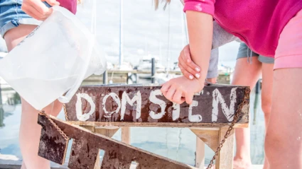 Närbild på skylt ("Domsten") och två barn som fiskar krabbor från bryggan i Domstens hamn i Helsingborg