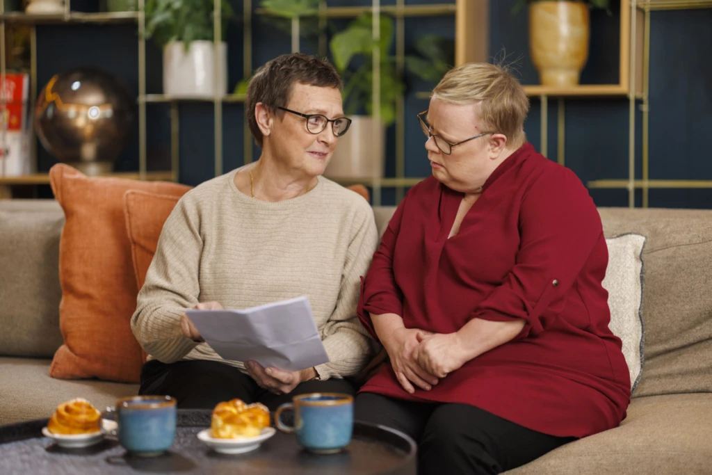 Två personer, Lena och Eva, sitter intill varandra i en soffa med ett papper i händerna