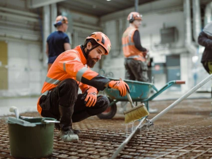 betongarbetare som arbetar på en byggarbetsplats. I bakgrunden ser man två andra män.