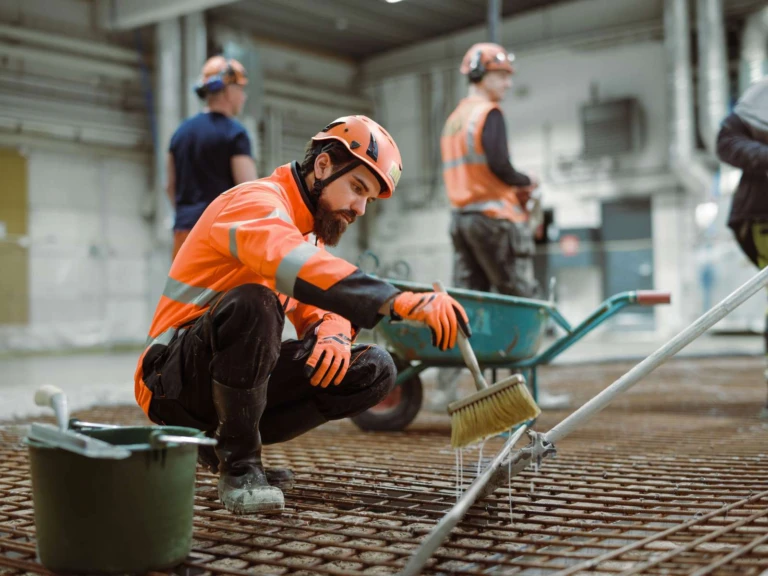 betongarbetare som arbetar på en byggarbetsplats. I bakgrunden ser man två andra män.