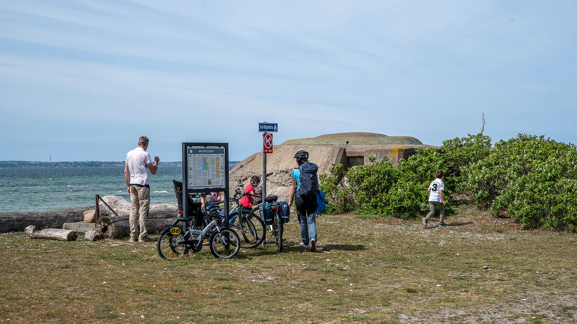 Personer på cykel vid naturreservatsskylt på stranden vid Örby ängar