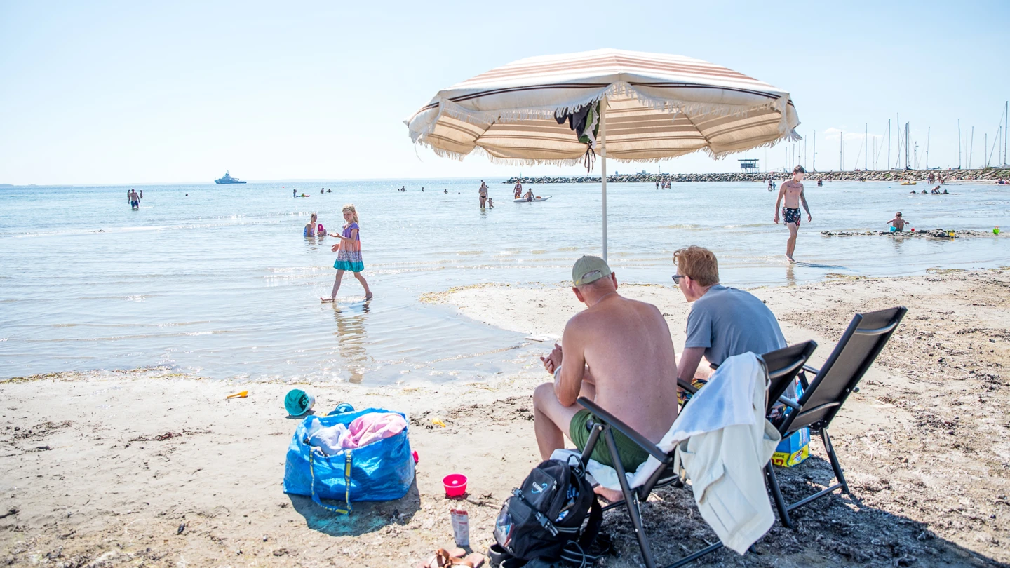 Personer under parasoll på stranden vid badplatsen Örby ängar norra