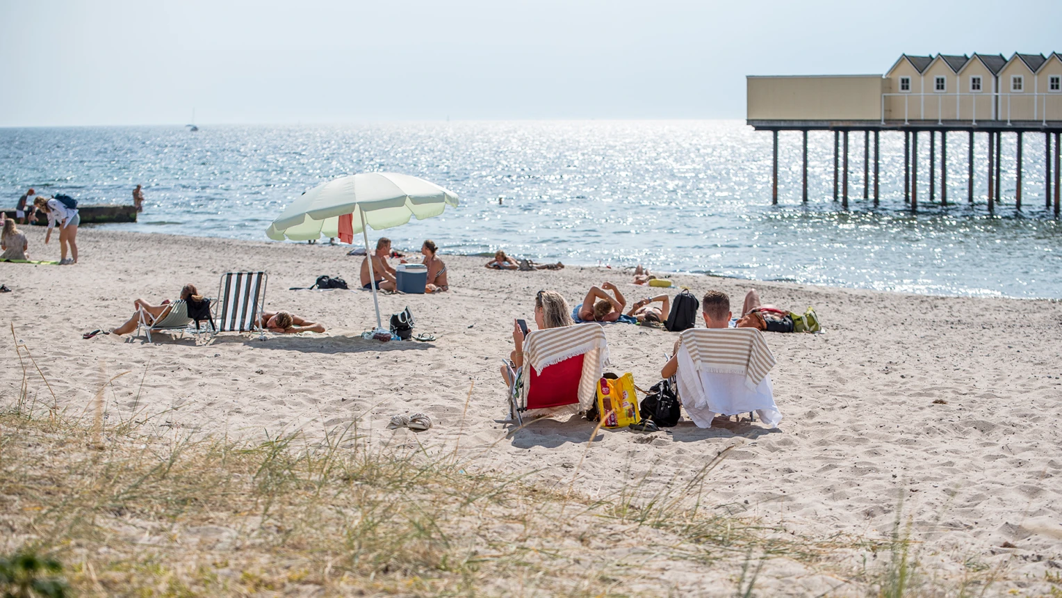 Personer som sitter på stranden vid badplatsen vid Pålsjö i Helsingborg