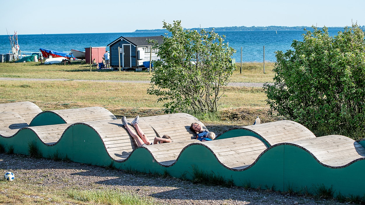 Vuxen och barn vilar på vilstolar i trä vid Råå vallar