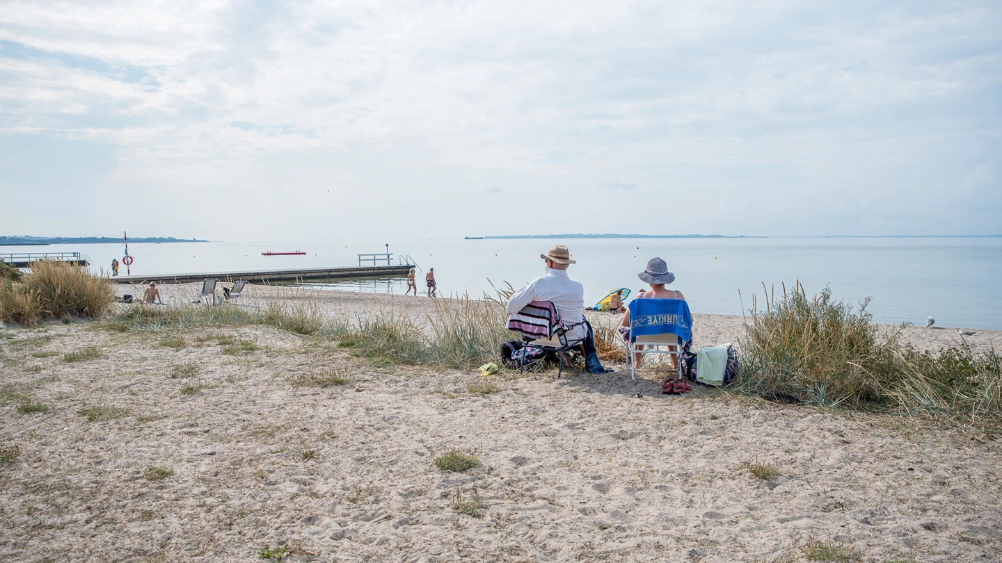 Två personer på stranden på Råå vallar tittar ut över badande och sundet