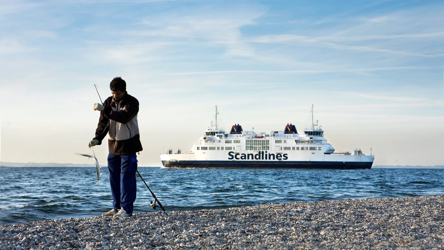 Man som fiskar på strand med färja utanför Helsingborg i bakgrunden (foto: Kim Nilsson/Studio-e)