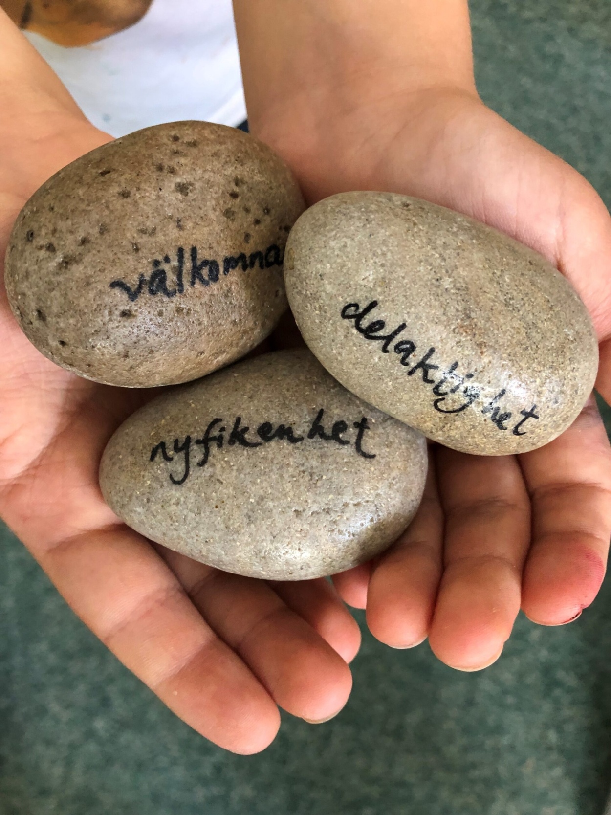 Tre stenar i hand med texten "Välkommen", "delaktighet" och "nyfikenhet
