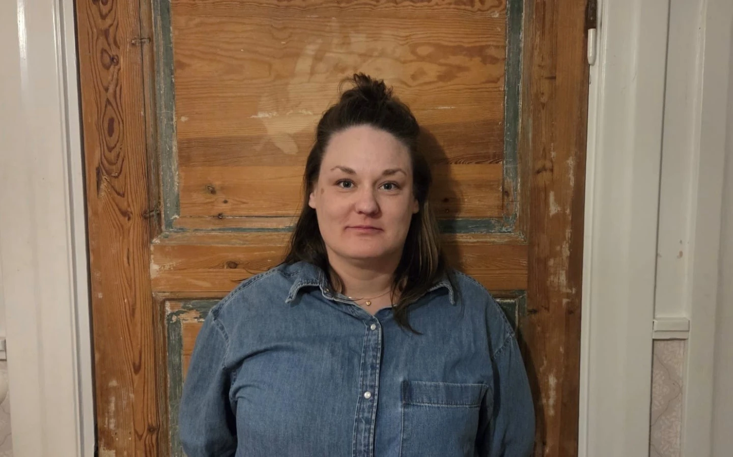 Bild på en kvinna i jeansskjorta mot en vägg av trä