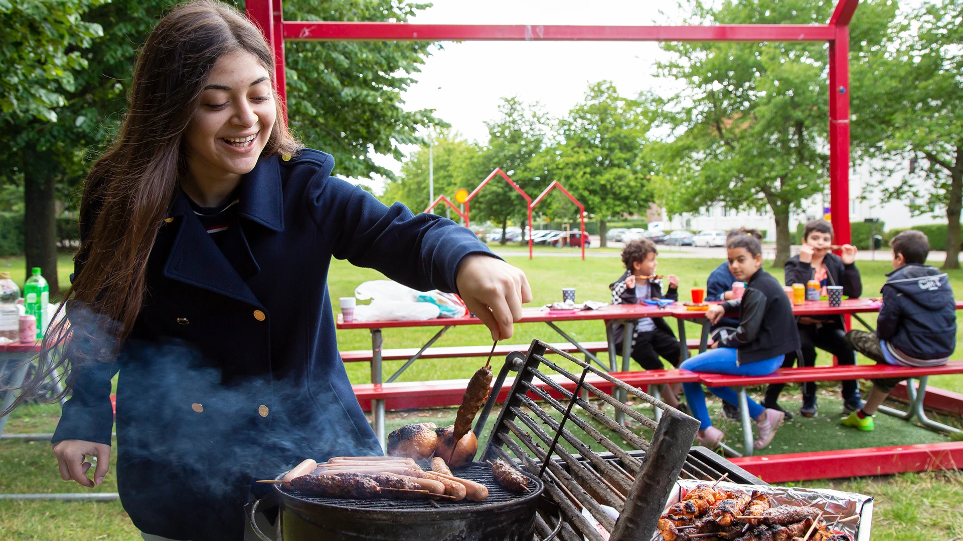 Flicka som grillar på grillplats på Viskängen, med barn i bakgrunden.