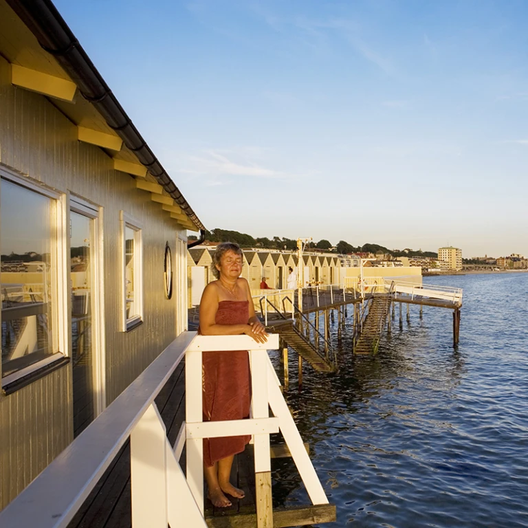 Kvinna klädd i handduk står och solar på bryggan vid Pålsjöbaden. Foto: studio-e.s