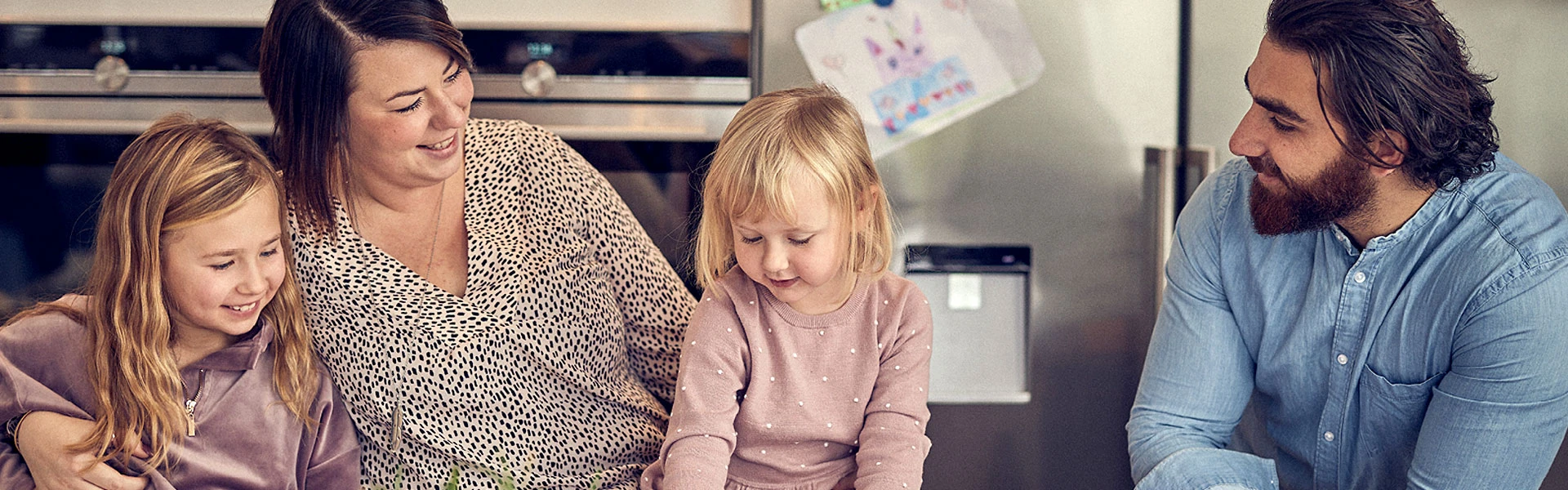 Familj med två vuxna och två barn sitter vid ett köksbord och ritar.