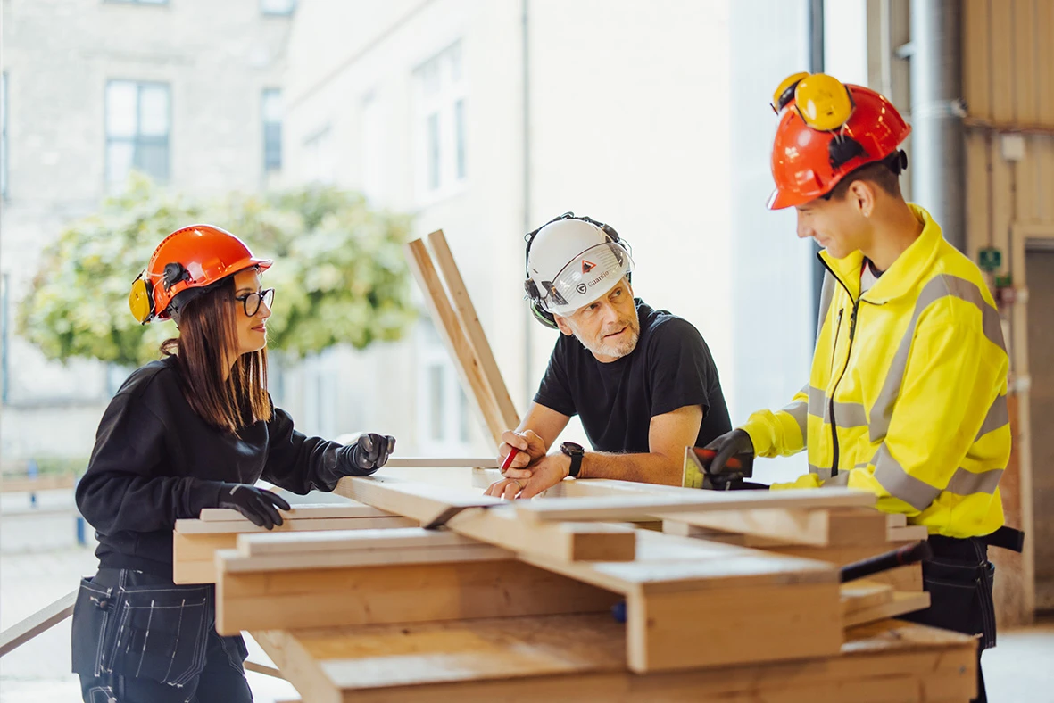 tre glada personer i bygghjälm som pratar med varandra