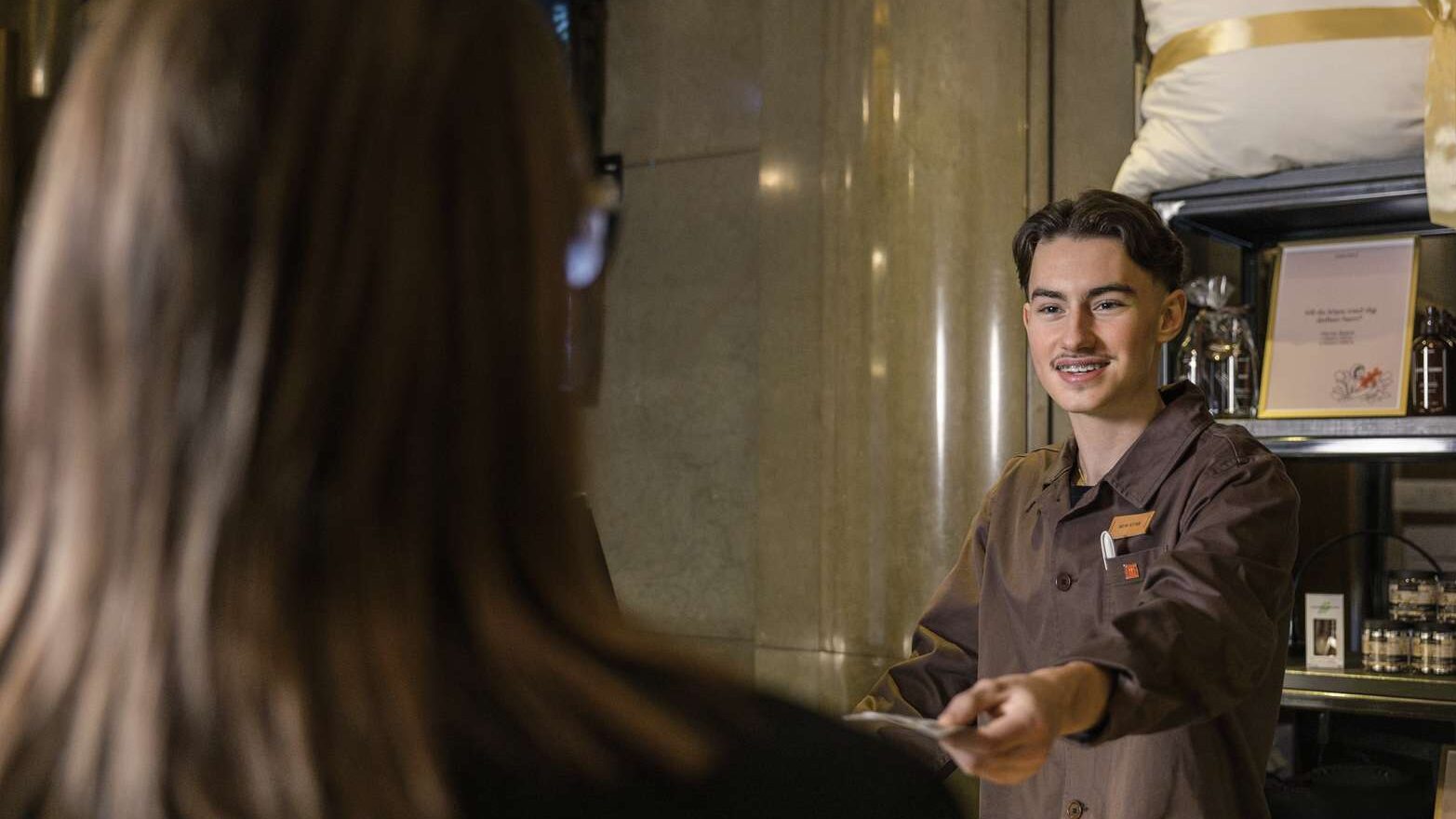 En receptionist räcker över ett nyckelkort till en person som syns i förgrunden.