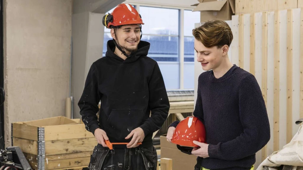 Två byggarbetare ler och pratar med varandra medan de tittar på en byggritning.