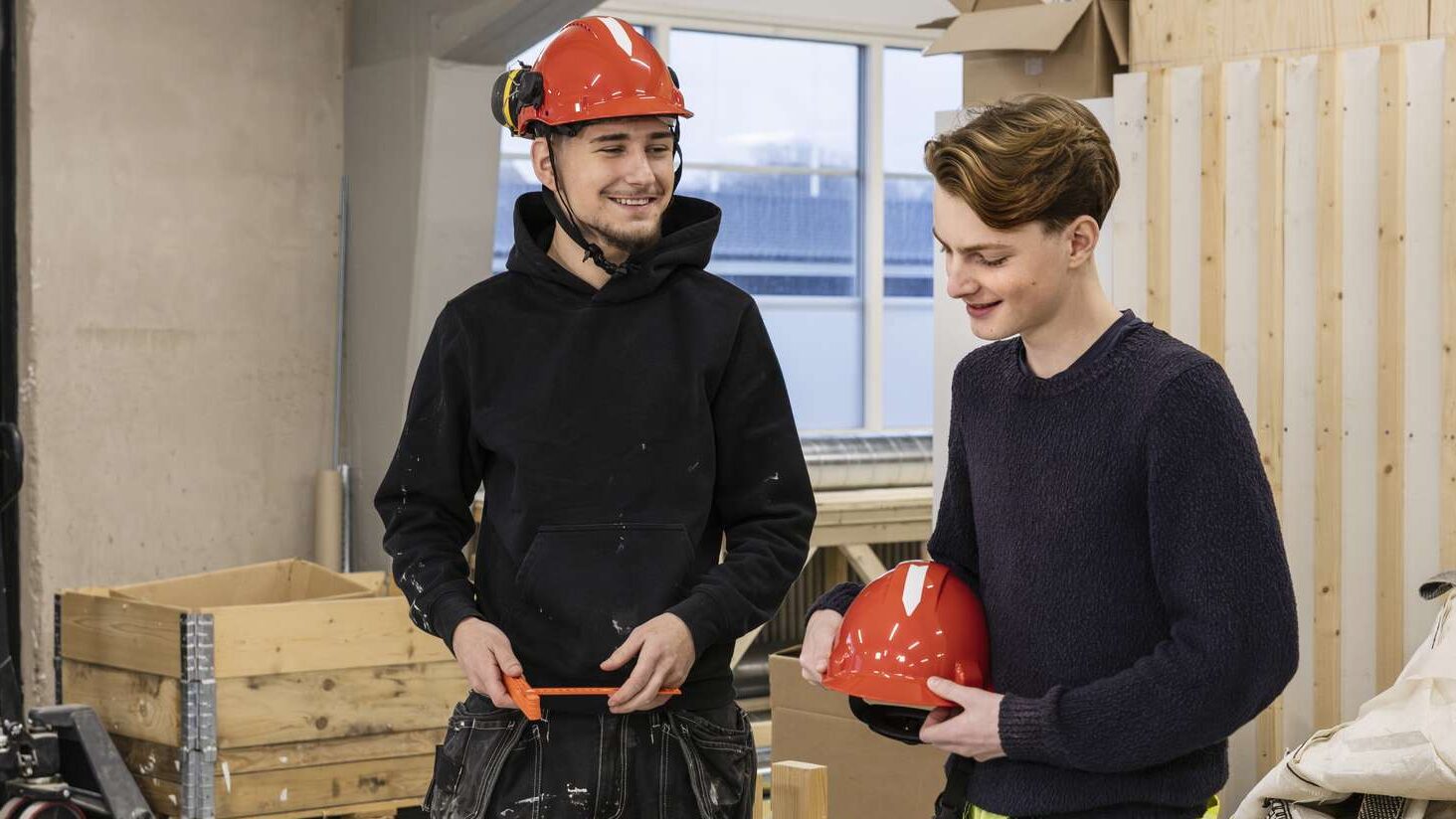 Två byggarbetare ler och pratar med varandra medan de tittar på en byggritning.