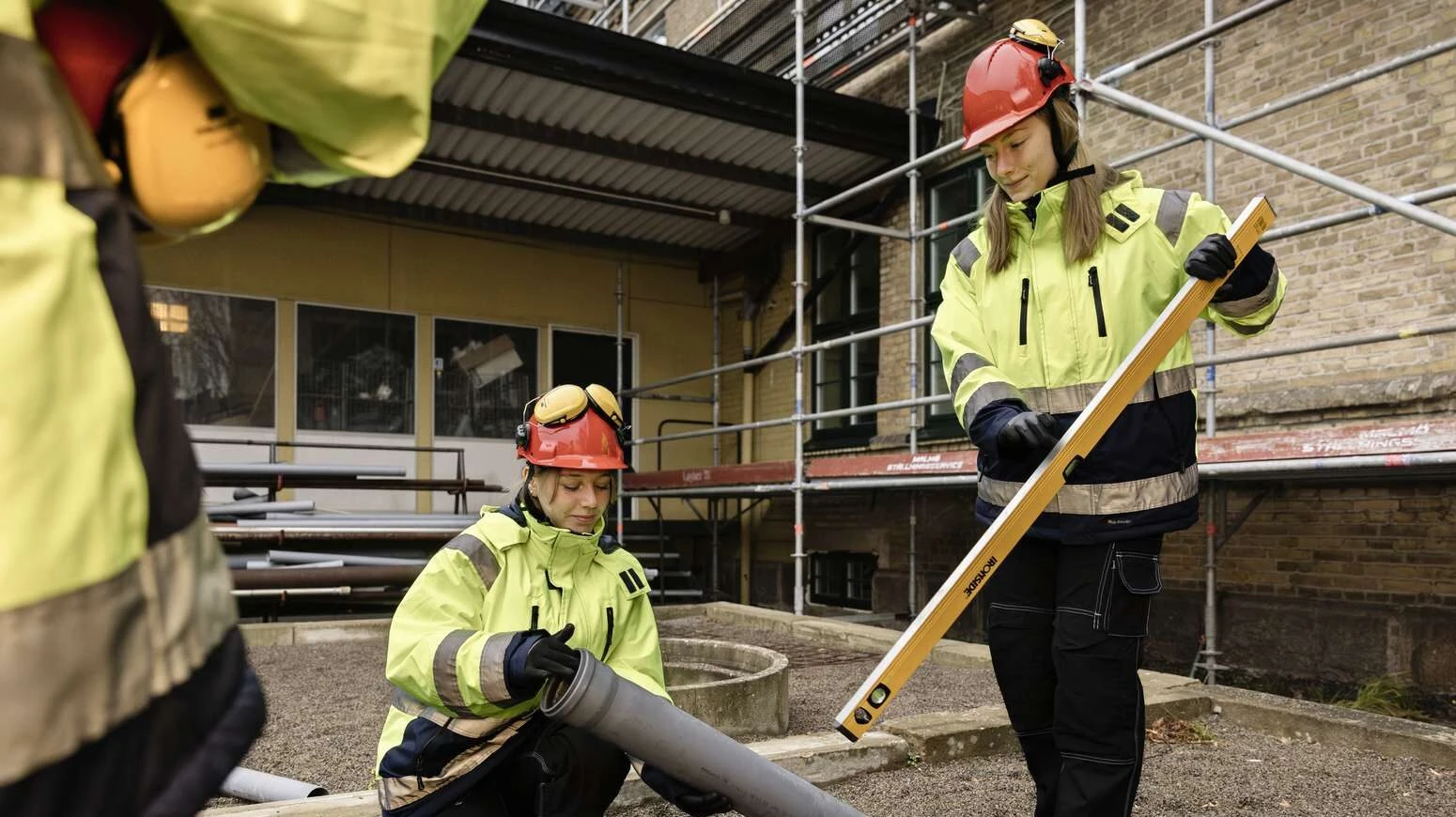 Två vvs-arbetare iklädda varselkläder lägger ner rör i sand.