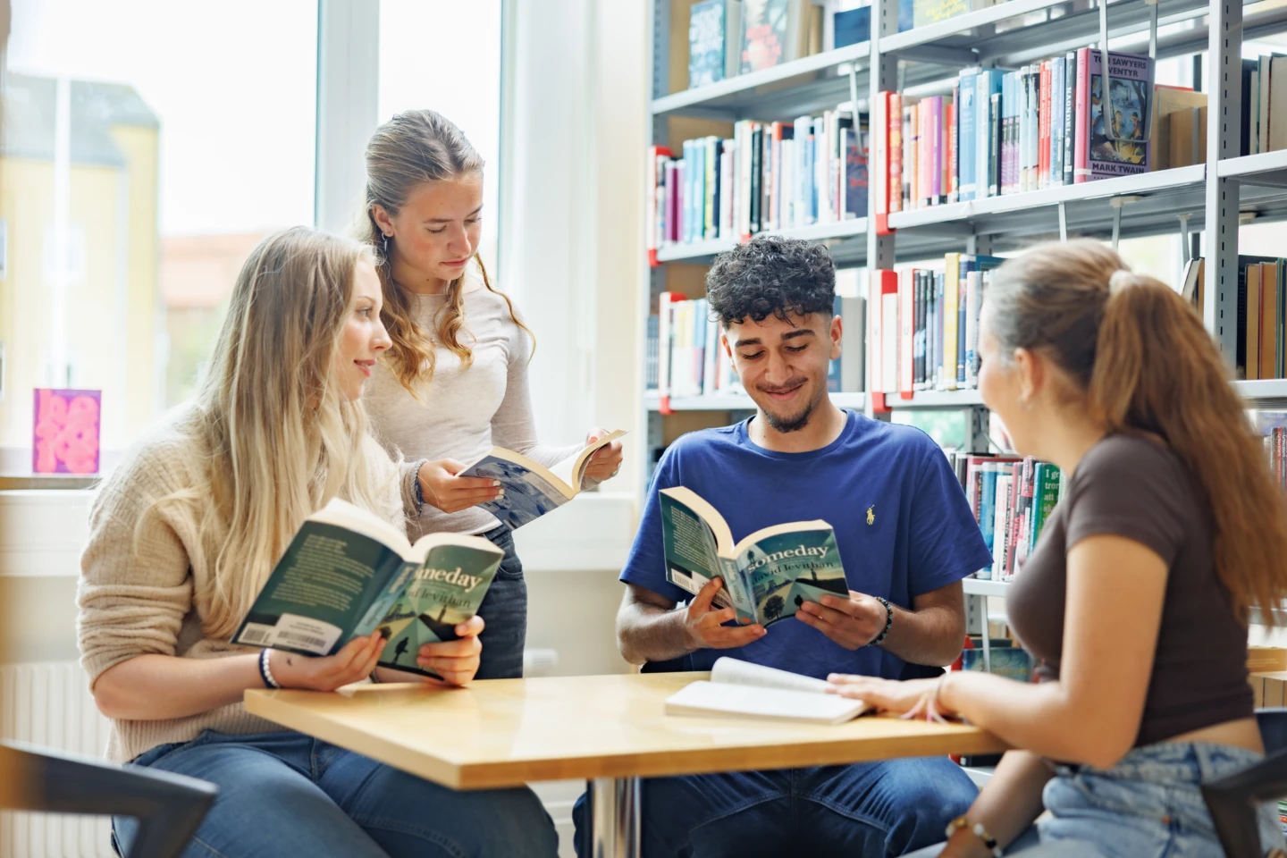 Skolungdomar läser böcker i ett skolbibliotek.