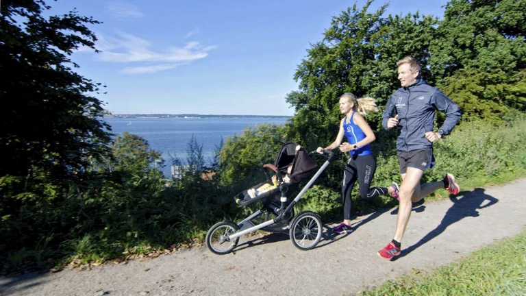 Ett par joggar längs stranden med en barnvagn.