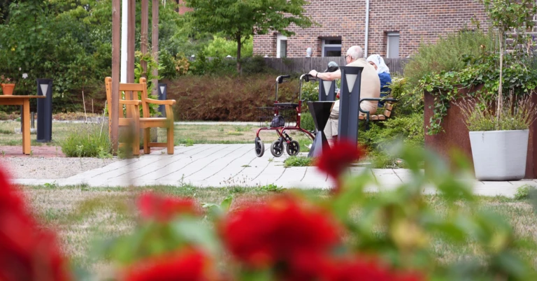 Ett äldre par som sitter på en bänk i en trädgård.