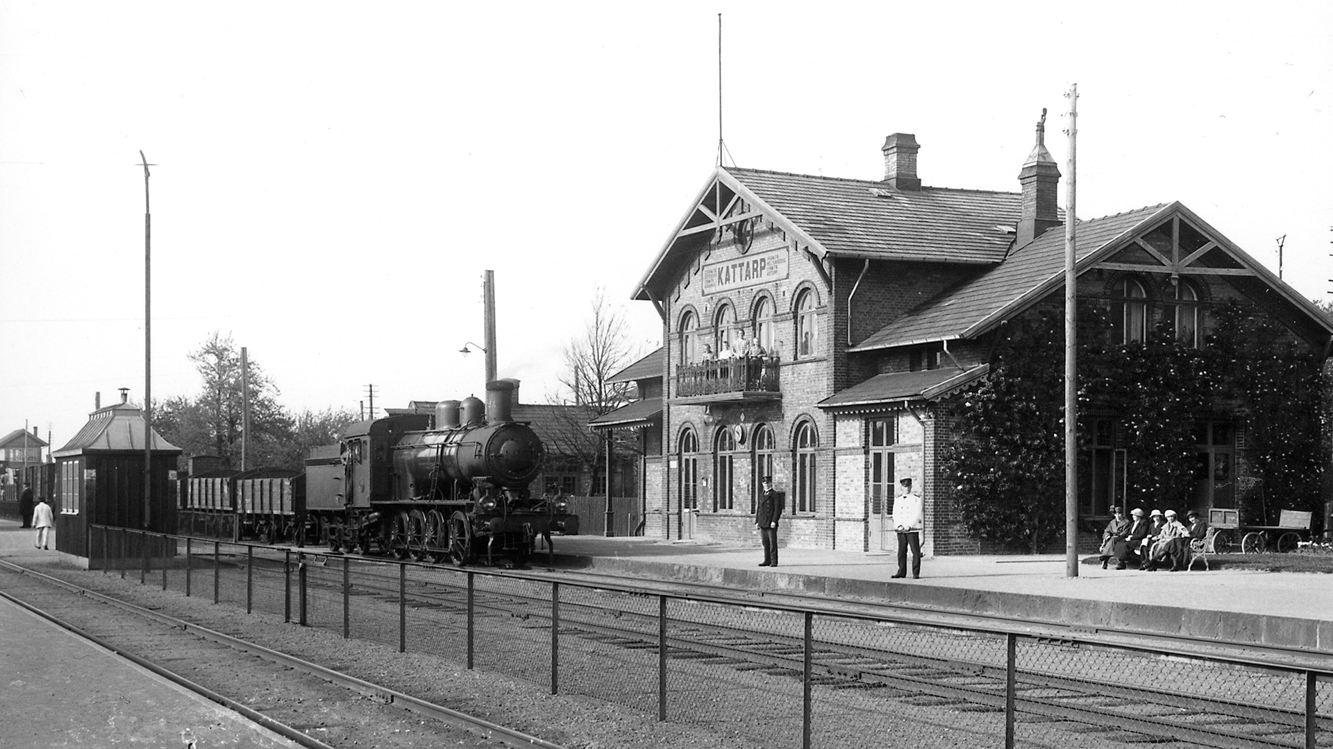 Kattarps stationshus 1928. Ett tåg med ånglok rullar in på stationen till väntande passagerare.