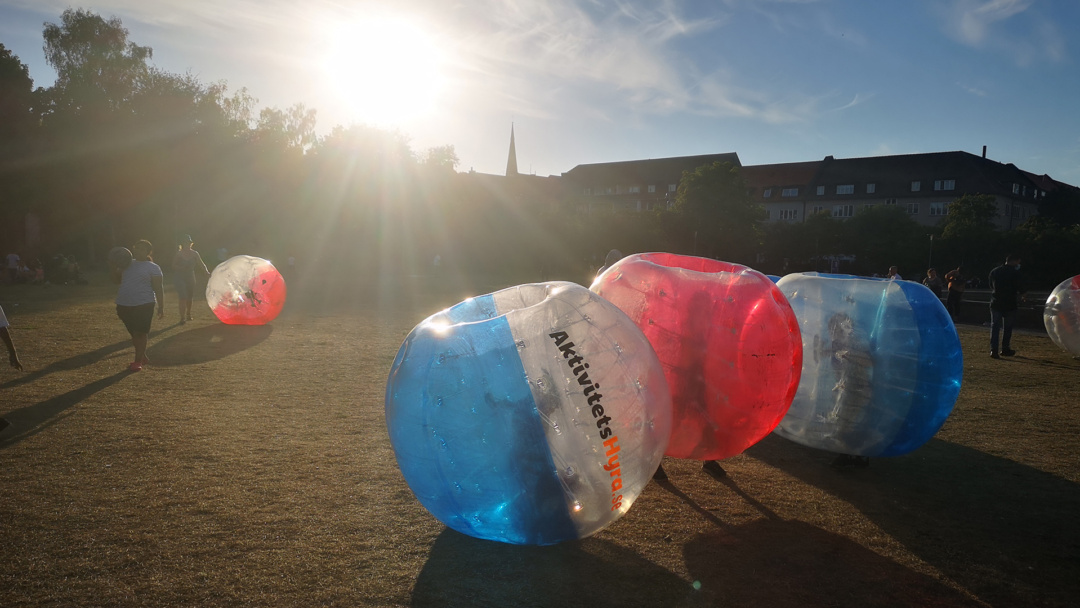 Personer i bubble ball-dräkter spelar fotboll i en park