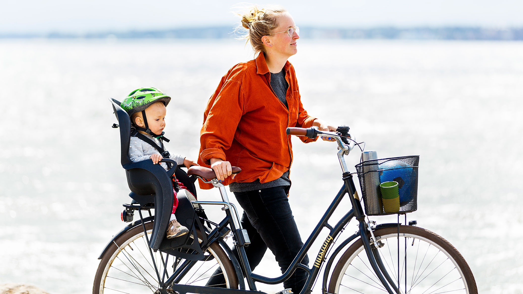 Person som leder sin cykel med ett barn som sitter i cykelstol.