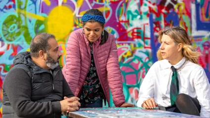 Tre personer pratar framför en graffiti-målning.