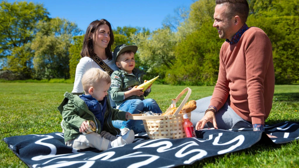 Två små barn har picknick i det gröna tillsammans med sina föräldrar.