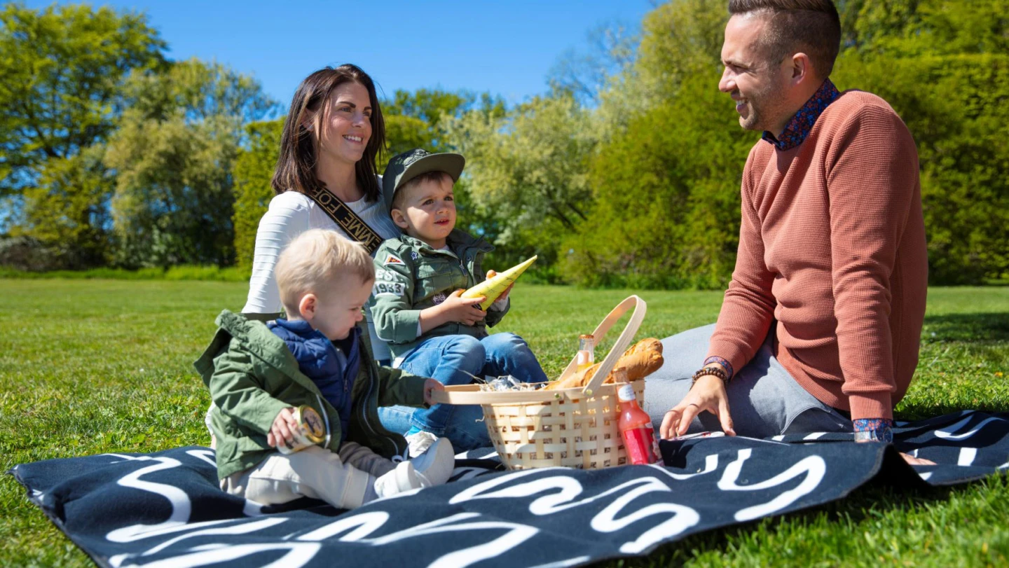 Två små barn har picknick i det gröna tillsammans med sina föräldrar.