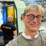 En leende Anders Gleerup tar en selfie i fabriksmiljö.