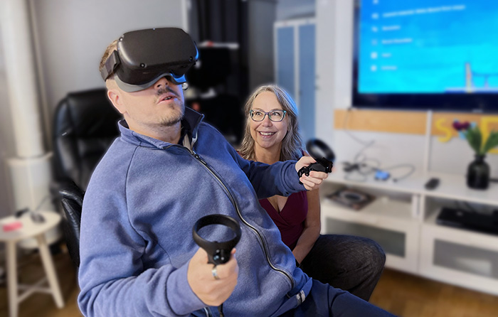 En kvinna ler och tittar på en man som har VR-glasögon på sig.