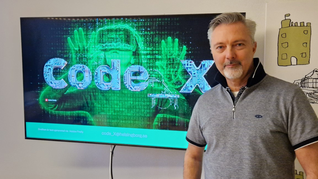 En man står framför en TV-skärm med texten Code_X