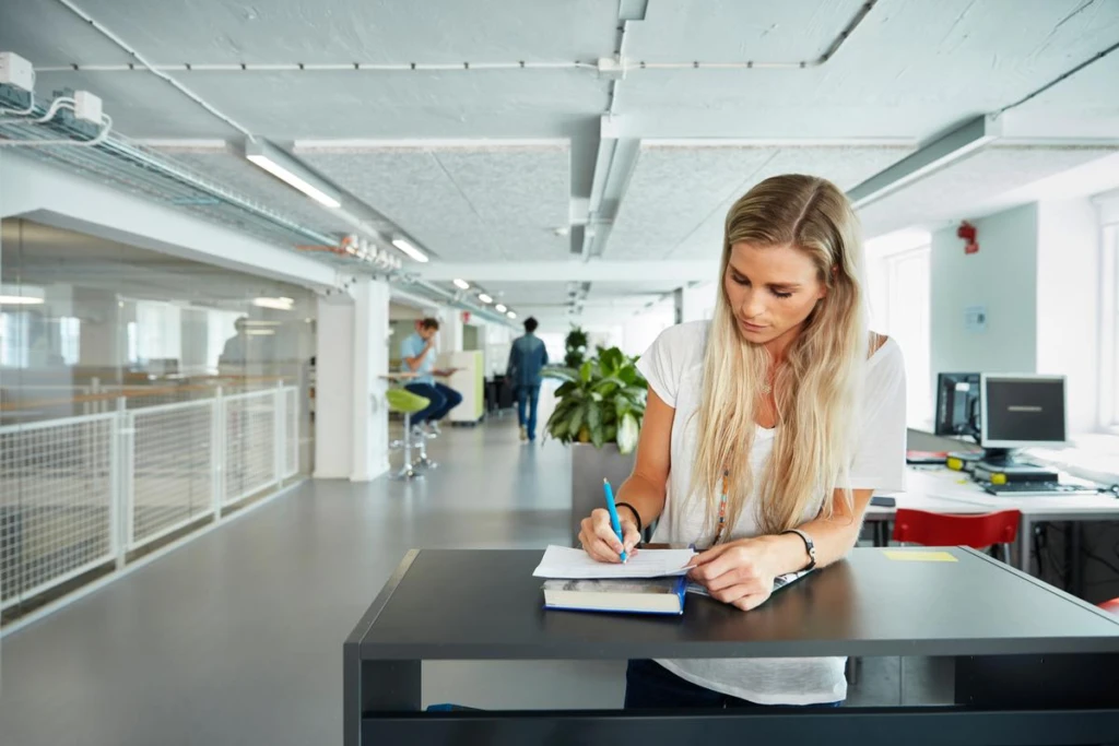 Tjej som står vid ett bord och skriver i en bok