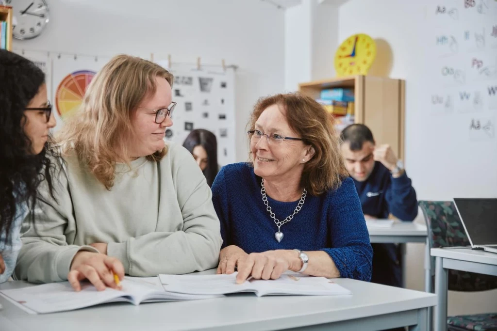 Kvinnor som sitter vid ett bord och läser ur en bok och ler