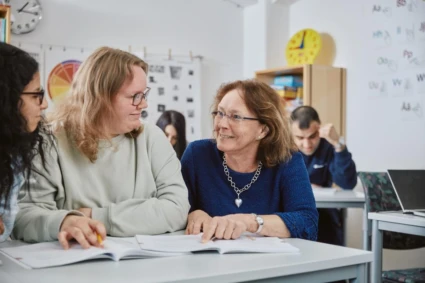 Kvinnor som sitter vid ett bord och läser ur en bok och ler