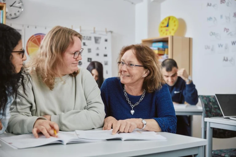 Kvinnor som sitter vid ett bord och läser ur en bok och ler