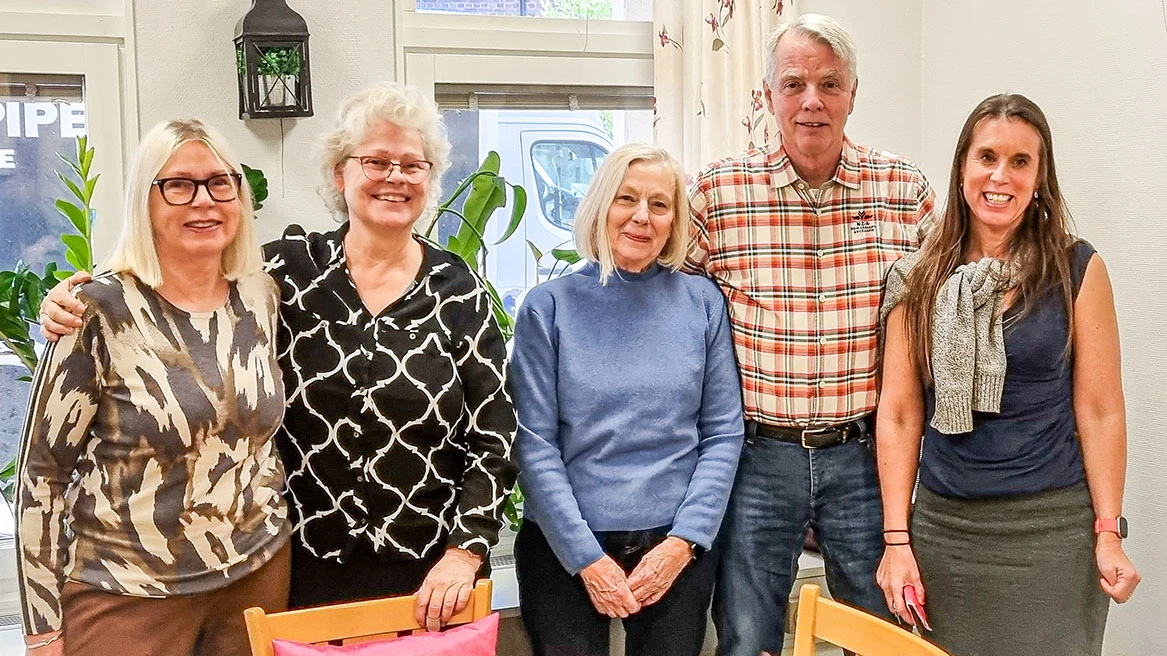 Fem personer står på rad, håller varandra om axlarna och ler mot kameran.