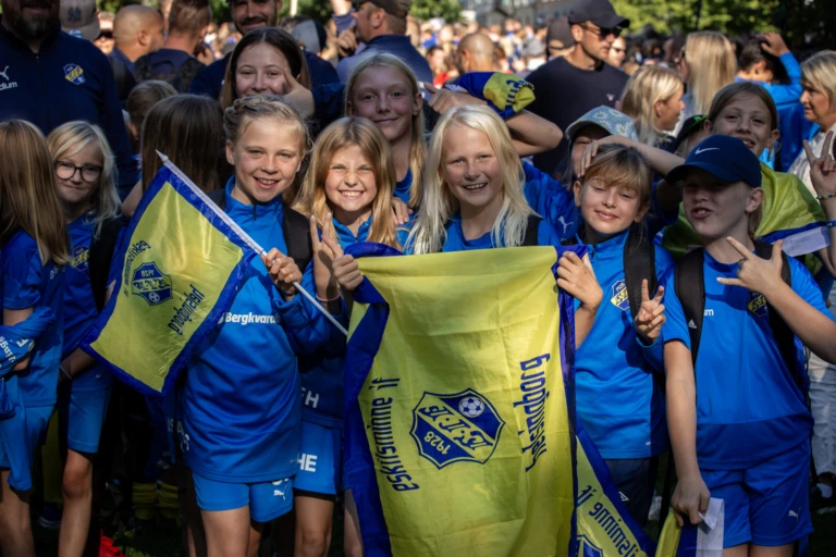 Fotbollsspelande barn från Eskilsminne IF samlade på en gruppbild under Eskilscupen, där de håller upp klubbens flagga.