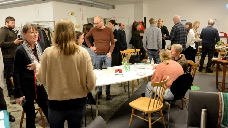 En grupp männikskor står och pratar runt ett vitt bord under en klimat_AW med Helsingborgarnas klimatavtal.