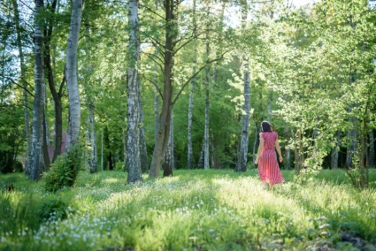Kvinna i röd klänning går i en solig, grön skogsglänta.