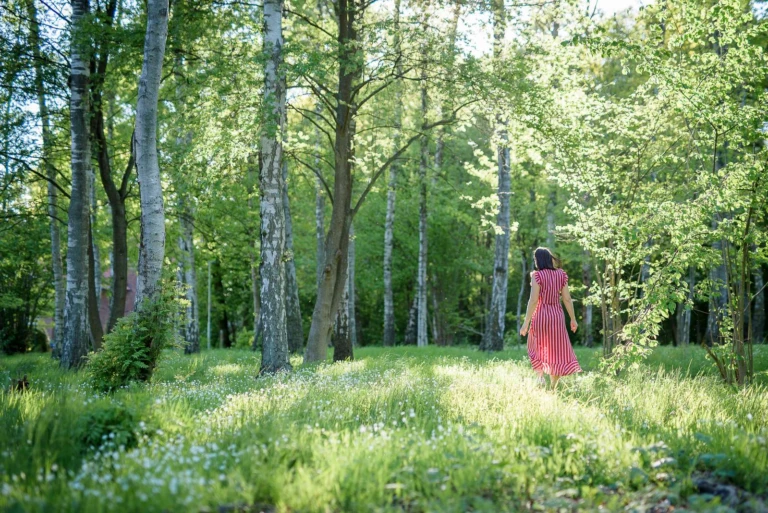 Kvinna i röd klänning går i en solig, grön skogsglänta.