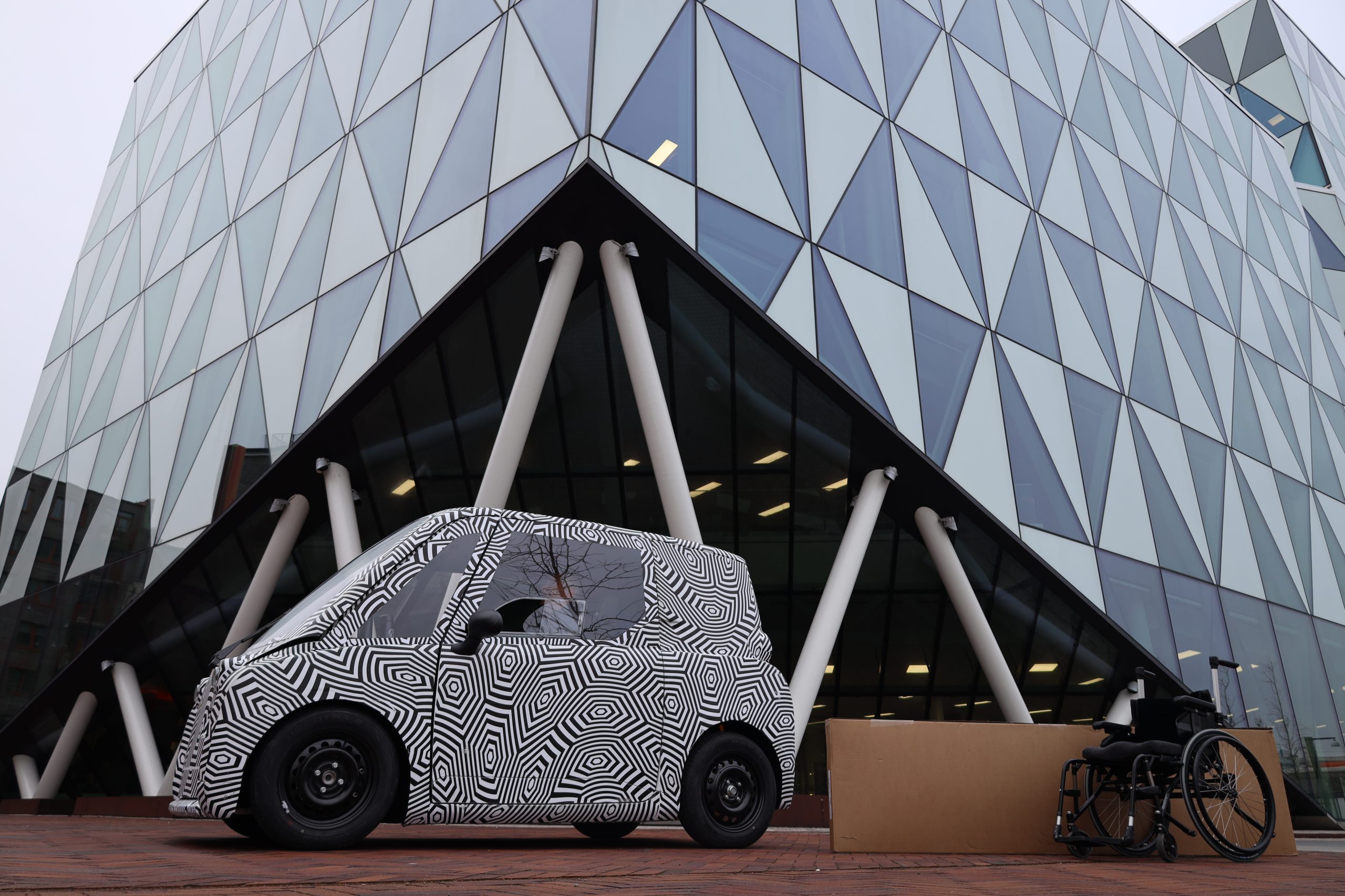 Ett zebrarandig bil står parkerad framför entrén till Prismahuset i Oceanhamnen, täckt av glaspartier.