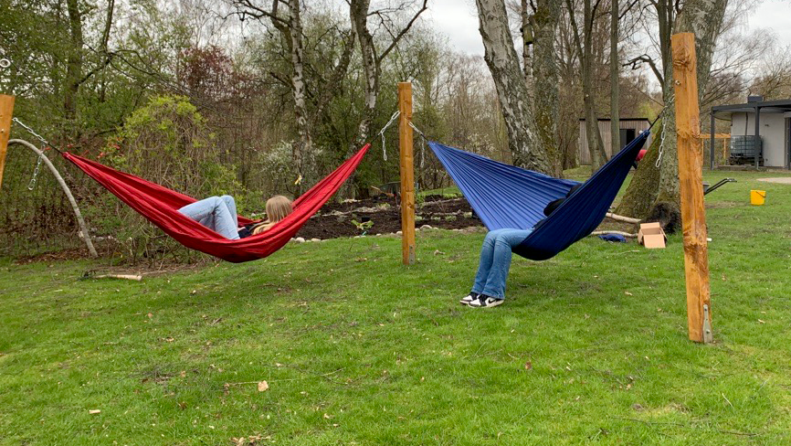 Två barn hänger i en röd och en blå hängmatta bredvid varandra.