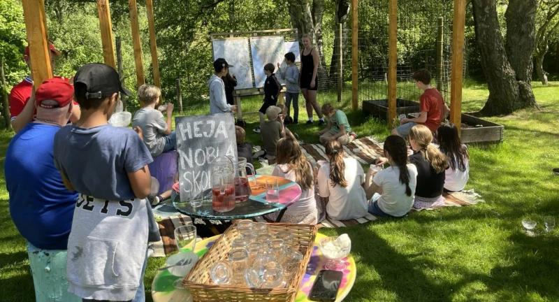 Elever samlade under en pergola ute på en grön gräsmatta.