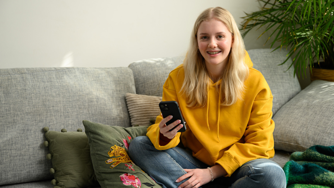 Flicka i soffa med Skånetrafikens app i telefonen.
