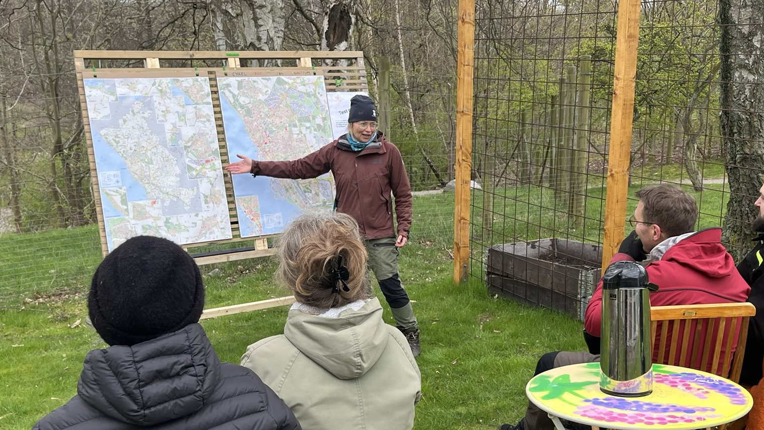 En pedagog står framför en uppfällbar trätavla utomhus.