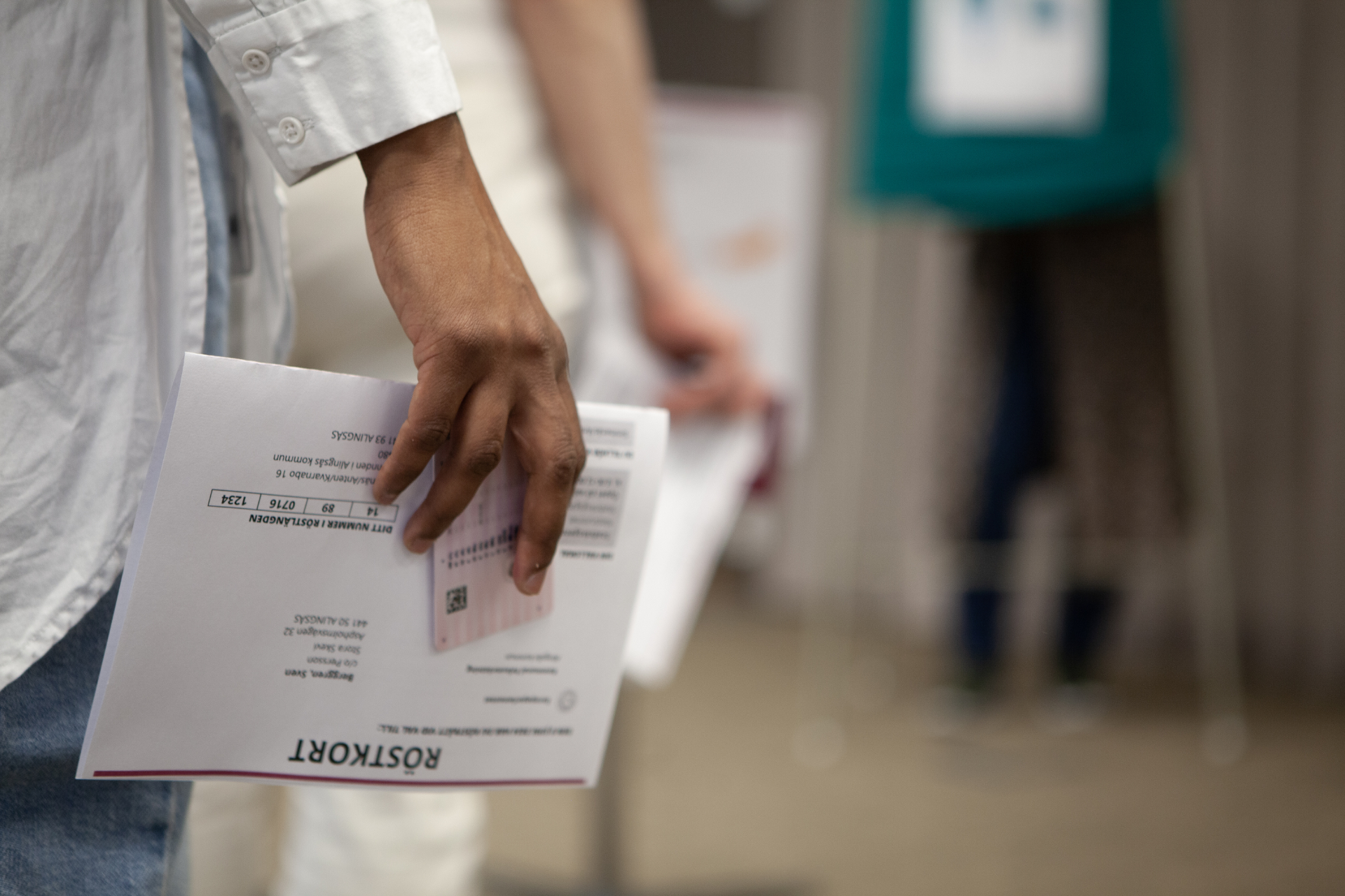 En hand håller i ett röstkort och ett körkort, till synes stående i en kort kö till ett valbås.