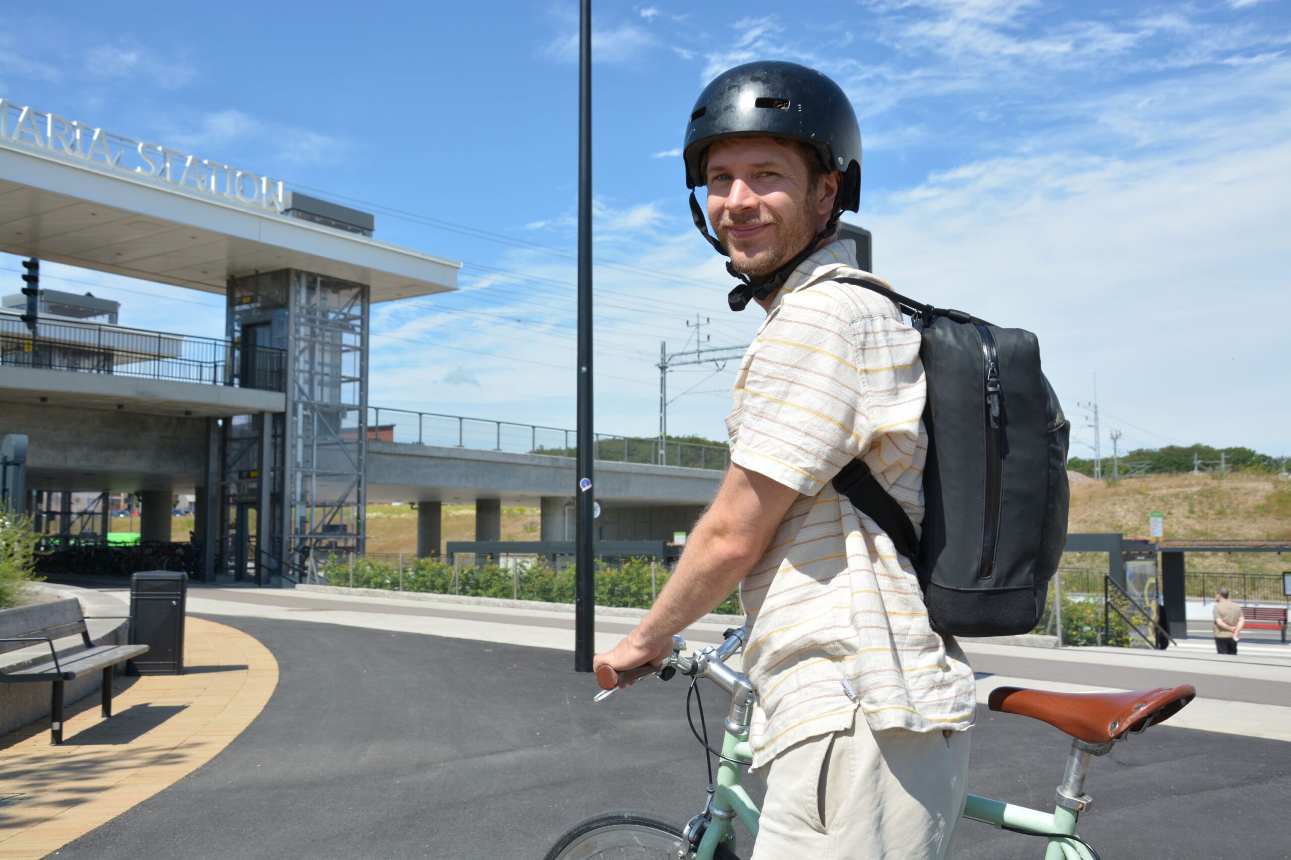 Man med cykelhjälm står håller i cykel framför Maria station.