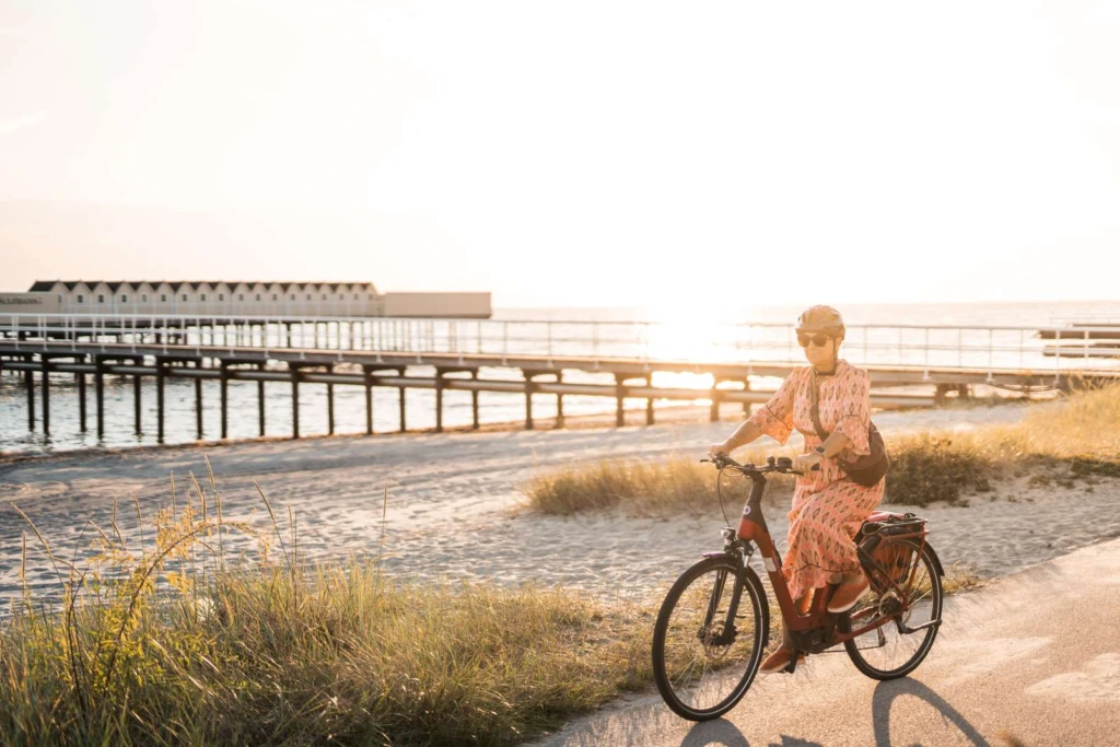 Kvinna i rosa kjol cyklar i solnedgången utmed havet vid Pålsjöbadet.