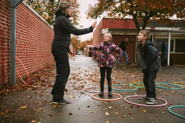 En vuxen och två barn leker på skolgården